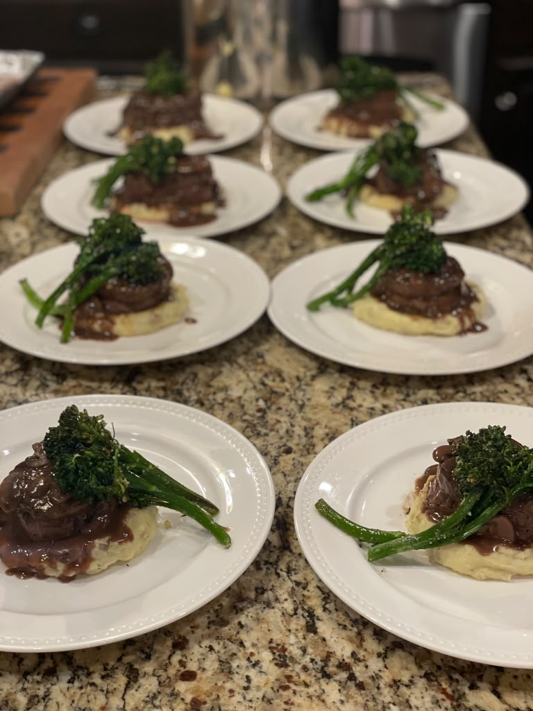 Row of plated filet mignon with mashed potatoes and broccolini